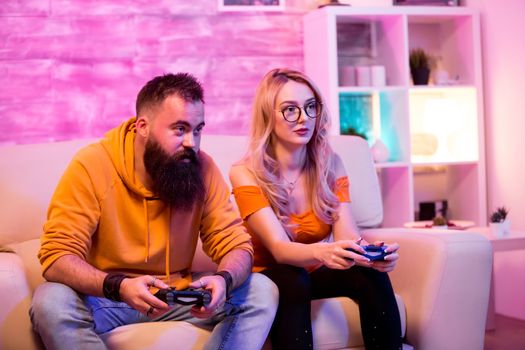 Beautiful young couple relaxing while playing online games together. Cheerful couple. Room with neon light.