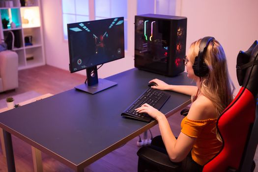 Girl relaxing playing games on computer and sitting on a gaming chair. Room with colorful neon light.