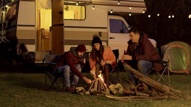 Friend of a couple helping to light the camp fire. Retro camper van. Light bulbs in the background.