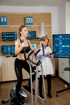 Female athlete who runs tests on the stepper and has electrodes on it and the doctor follows on his tablet and screen his evolution. Clinical tests