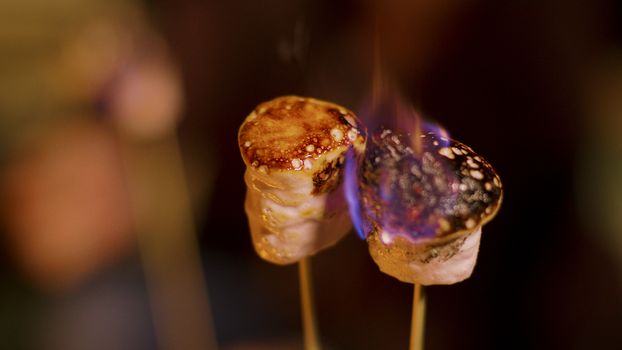 Close up of delicious marshmallow on sticks roasting. Cold night of autumn.