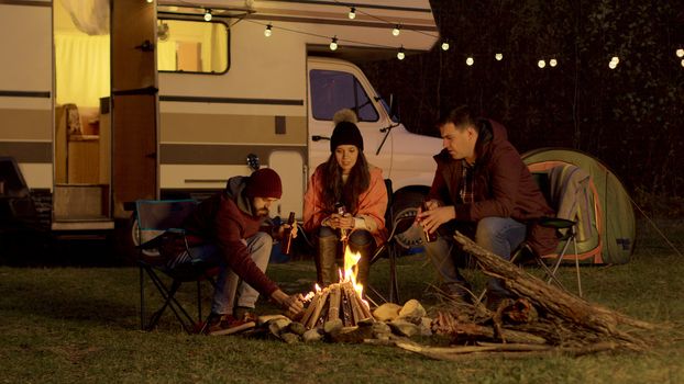 Friend of a couple helping to light the camp fire. Retro camper van. Light bulbs in the background.