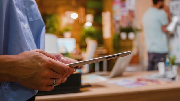Woman hands holding a digital tablet in creative space. Loft office in the background