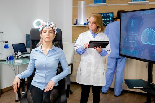 Doctor doing a girl's brain scan procedure in a scientific lab. Brain waves scanning helmet