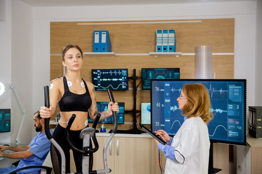 Female patient giving physical activity tests in the lab while a doctor supervises her. Test with electrodes
