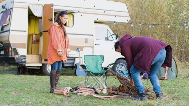 Cheerful couple preparing the wood for camp fire. Retro camper van. Camping tent.