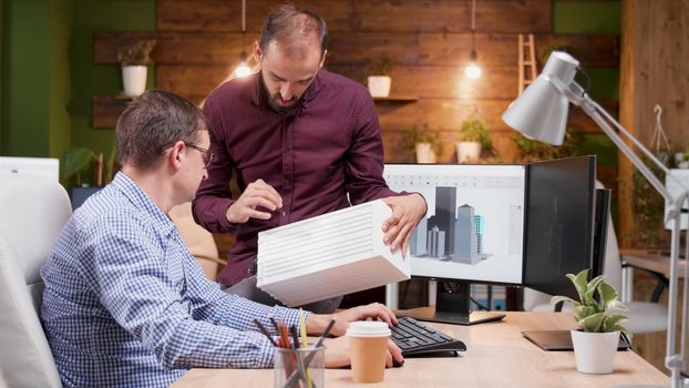 Architect in the office talking about the engineering for the new building structure with his assistant.
