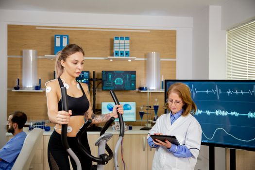 Female athlete running tests on the stepper and doctor making notes in tablet. Test with electrodes
