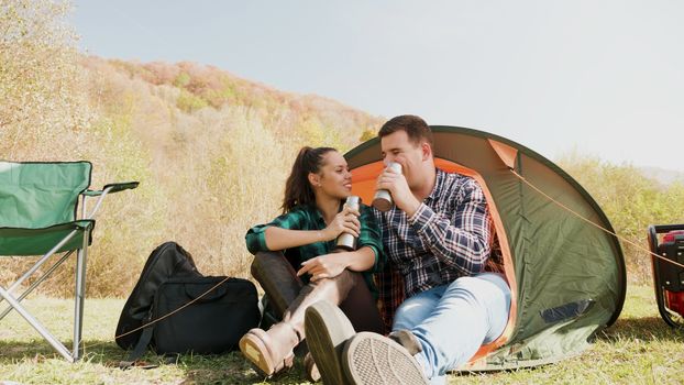 Couple enjoying a drink together in front of their camping tent. Camping chairs. Camping generator.