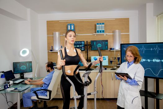 Female athlete who runs tests on the stepper and the doctor follows her evolution and makes notes on the tablet. Test with electrodes