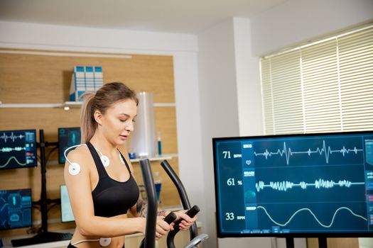 Female athlete who makes a physical effort on the stepper and has electrodes attached to it and the results are seen on the screen. Sports laboratory