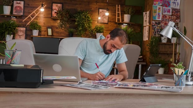 Young busy designer makes some notes on some printed pictures. Loft office and busy boy