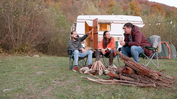 Bearded friend telling a story to his couple friends in front of camper van. Wood for fire. Friends relaxing.