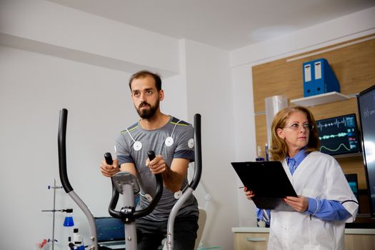 Male athlete who makes a physical effort on the stepper and has electrodes attached to him and the doctor who follows his evolution on the screen. Clinical tests