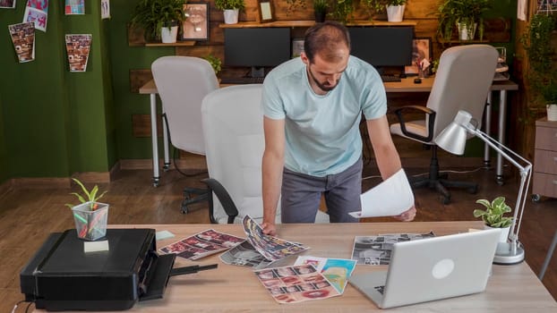 Caucasian young designer standing and looking through some printed pictures. Busy artist and creative job