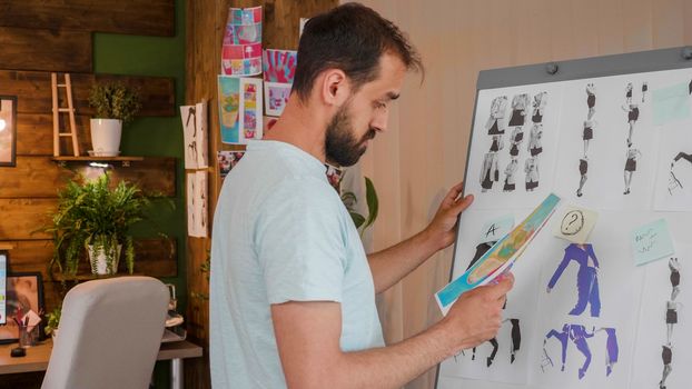 The designer boy looks at a printed picture that he holds in his hand near a whiteboard. Creative agency and modern office