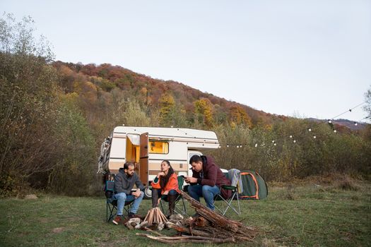 Group of friends camping together in the mountains wainting for the night to make camp fire. Retro camper van.