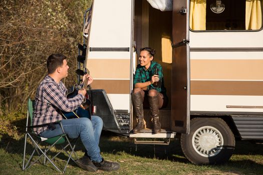 Hipster couple relaxing with a guitar song in front of their retro camper van. Couple relaxing in the mountains.