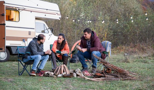 Caucasian friends camping together in mountains with their retro camper van. Setting up camp fire.