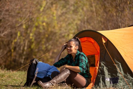 Young woman talking on the phone near a tent in the woods.Happy young woman