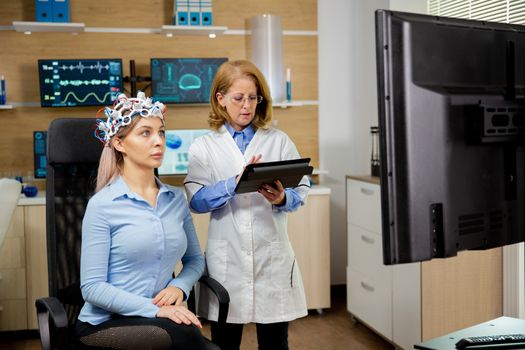Patient woman scanning her brain and doctor making notes in the tablet holding it in her hand. Brain waves scanning device