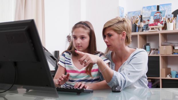 Young attractive woman helping a teenage girl with a text on computer. Mother helping her daughter to write a text.