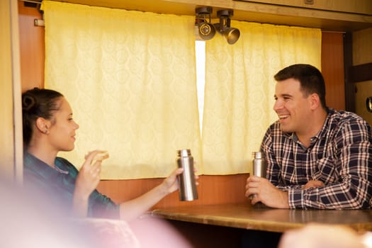 Couple of lovers enjoying a hot drink and a snack at the table in the retro camper. Vacation in nature