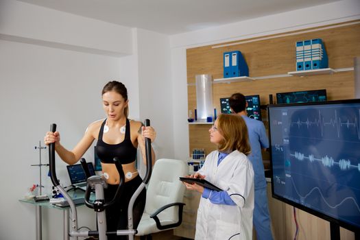 Female athlete doing physical effort on the stepper and the doctor follows her. Sports laboratory