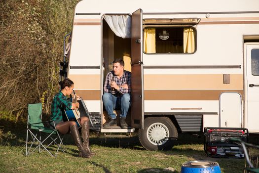 Beautiful young girlfriend singing for her boyfriend in front of their retro camper van. Happy couple.