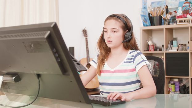 Girl playing on her computer an online game with her virtual friends. Teenage girl at a desk playing on a computer.