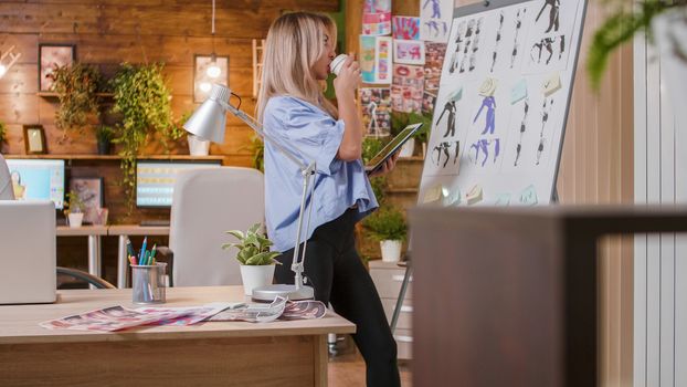 Young designer drinking coffee and looking at the whiteboard and following the evolution of the project. Creative work space