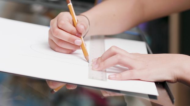 Young girls hands drawing a line on a piece of white paper using a ruler and a pencil. Preparing for fine art class at school.