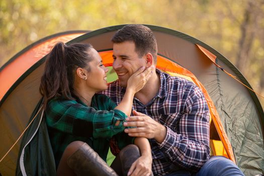 Loving couple smiling while looking at each other in front of the tent. Romantic atmoshere