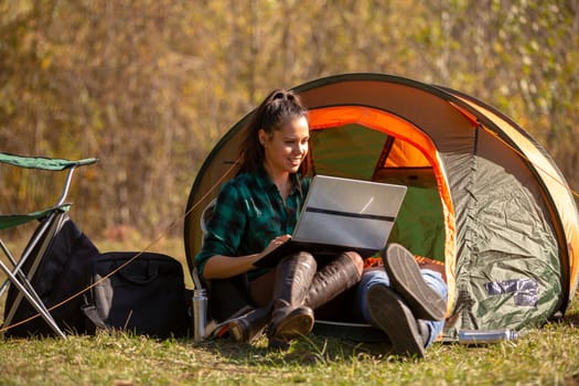 Young girl working on her friend's laptop next to the tent. Outdoor activity