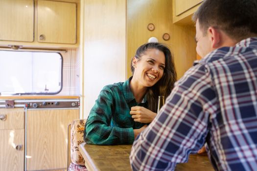 Young couple smiling and chatting while drinking beer in the caravan. Cool atmosphere