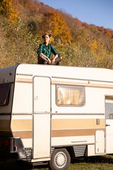 Young girl relaxing in autumn weighing on the roof of a retro camper. Young and beautiful girl