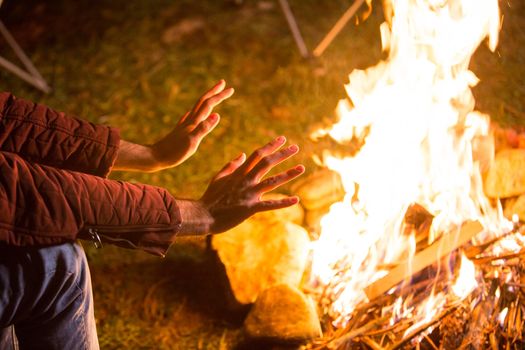 Tourist warming up his hands above camping fire in the mountains.