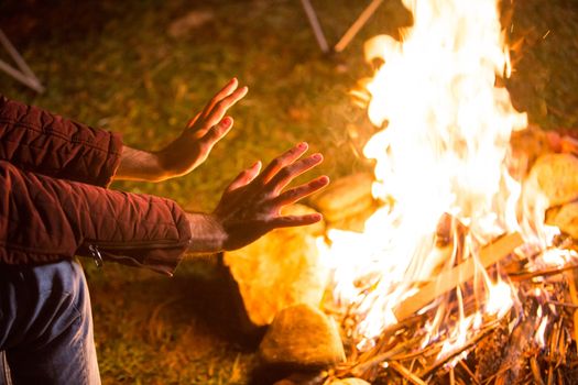 Man warming up his cold hand above camping fire in a campsite in the mountains.