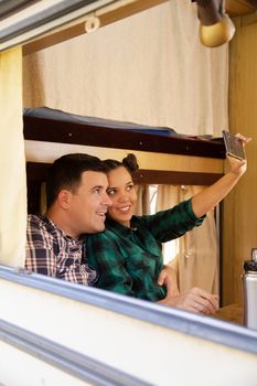 Hipster young couple relaxing together inside their retro camper van and taking a selfie.