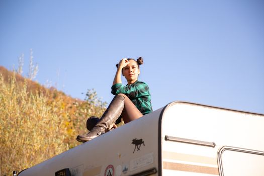 Young girl relaxing on the roof of a retro camper and looking around. Rebellious spirit