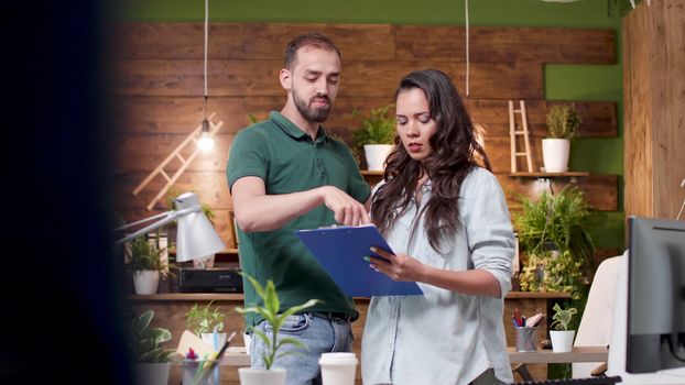 Two colleagues are debating over a new project while standing and looking at a clipboard