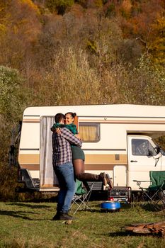 Cheerful couple having a moment of affection in front of their retro camper van. Couple relaxing together in campsite.