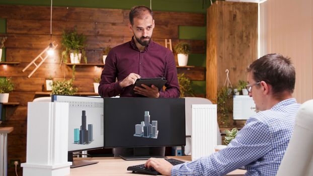 Architect sitting at his office explaning his assistant the building concept for the city.