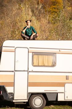 Pensively girl sits on the roof of a retro camper. Mountain adventure