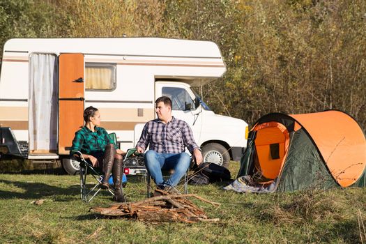 Beautiful young couple relaxing together in the mountains with their retro camper van in the background.