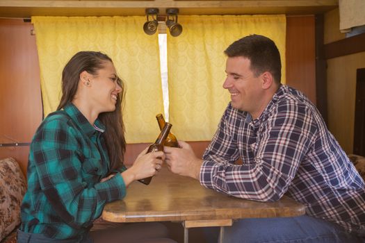Young couple smiling and clicking a bottle of beer in the camper van. Happy holiday