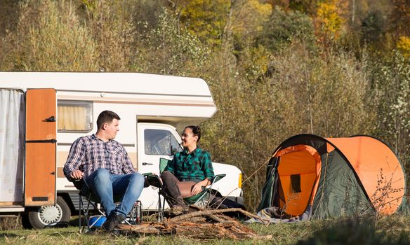 Couple relaxing in a campsite with their retro camper van in the background after a long journey.