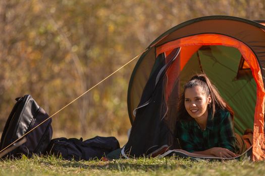 Smiling young woman standing in front of the tent. Forest background