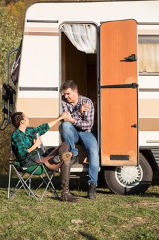 Woman sitting on camping chair and looking at her boyfriend sitting on the stairs of their retro camper van.
