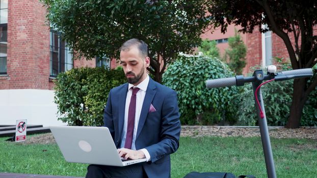 Young man in business suit working on the laptop out of the office in a business district. Slow motion footage